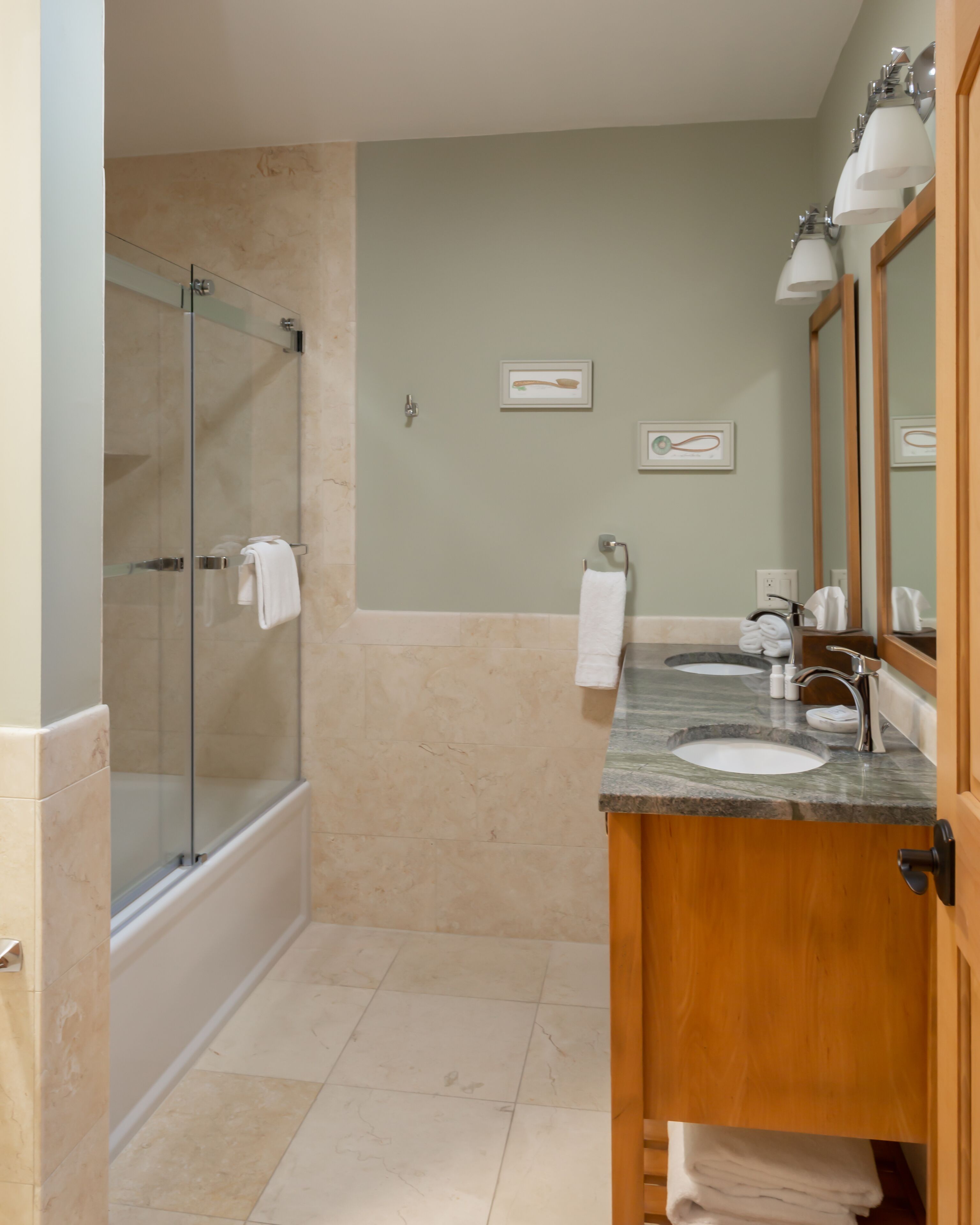 A bathroom with a glass-enclosed shower, two sinks with mirrors, and a wooden vanity.