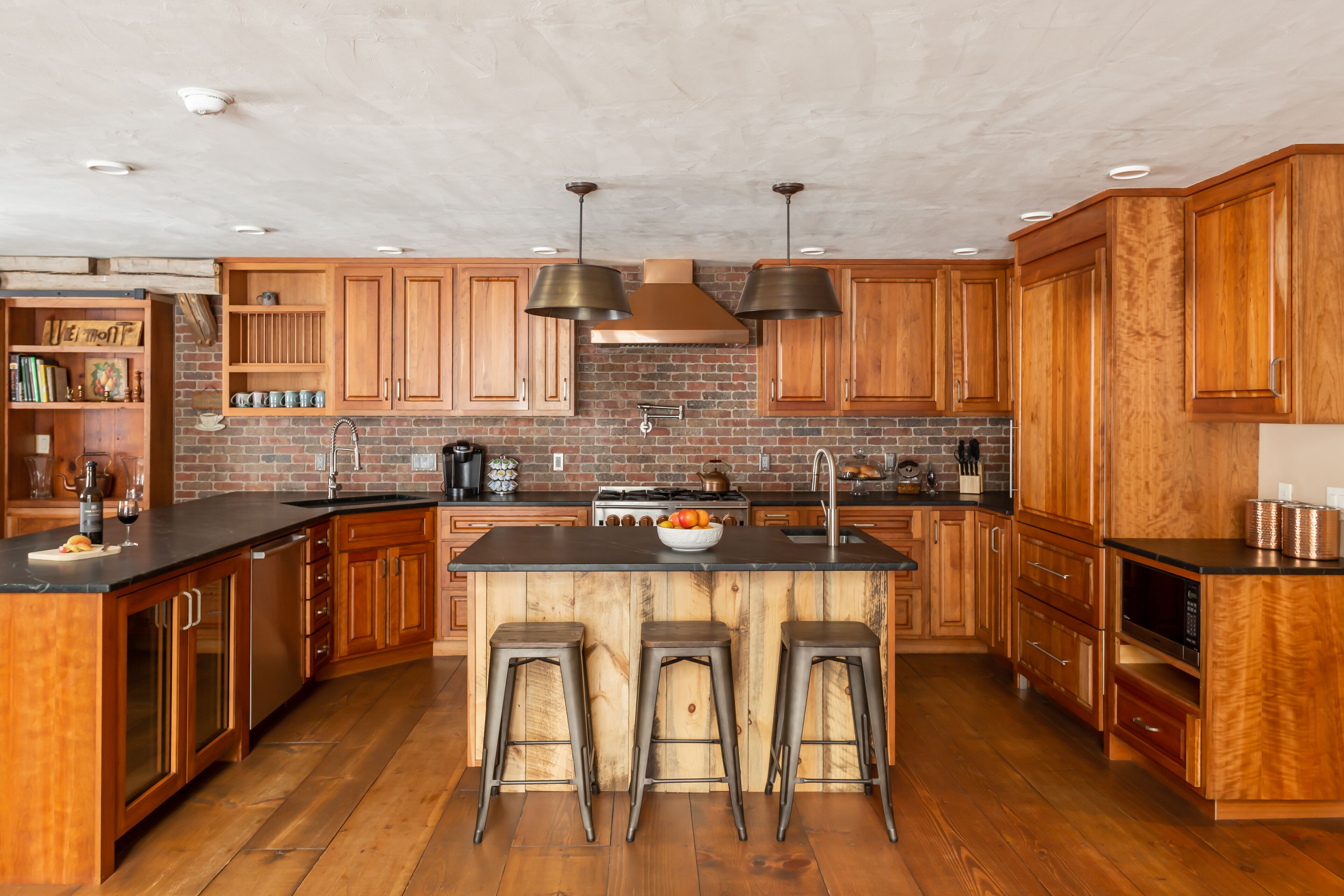 A spacious kitchen with wooden cabinets, a central island with stools, and a brick backsplash.