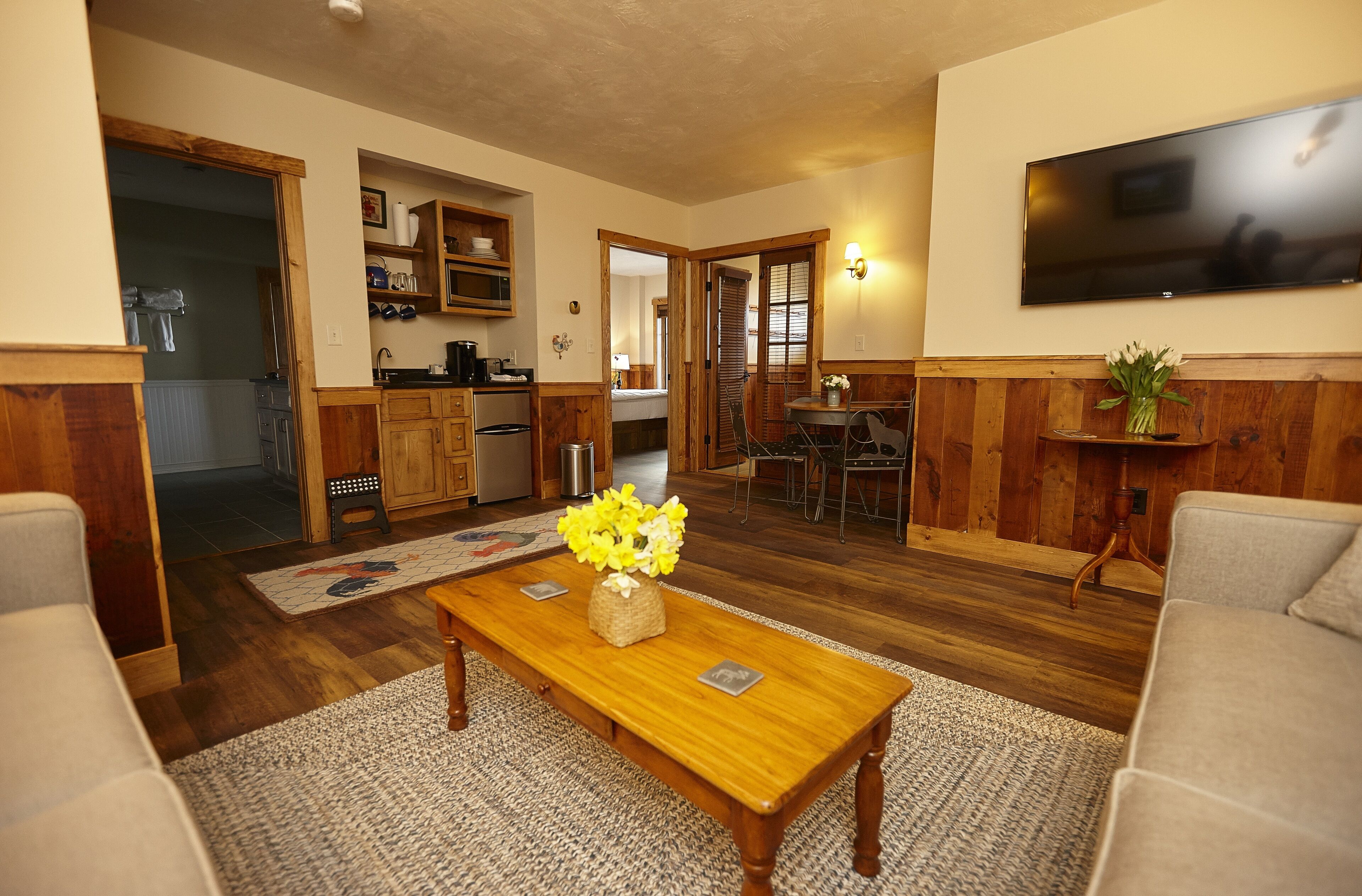 A living room with a wooden coffee table, a sofa, and a TV mounted on the wall.