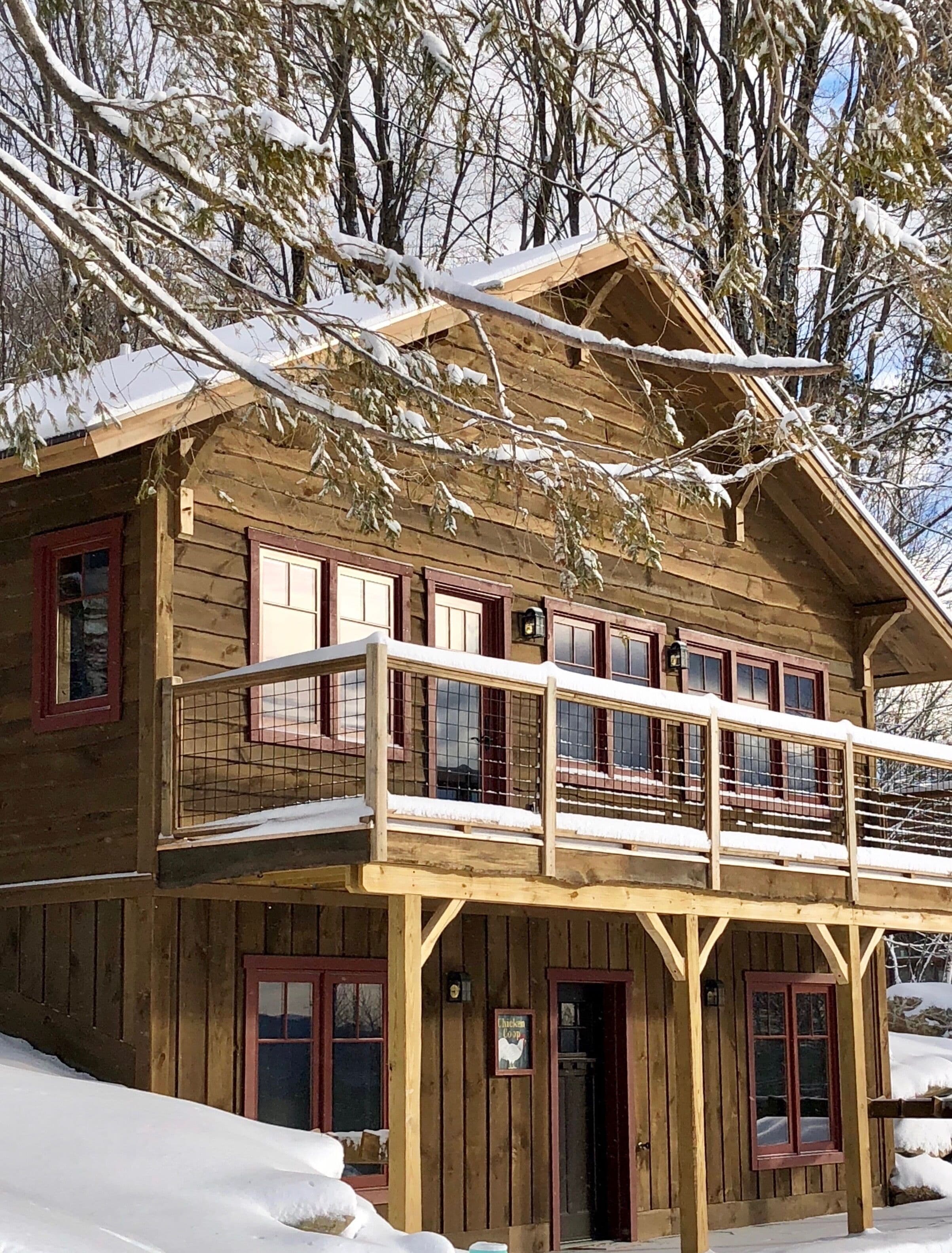 Una cabaña de madera con balcón, rodeada de árboles cubiertos de nieve.