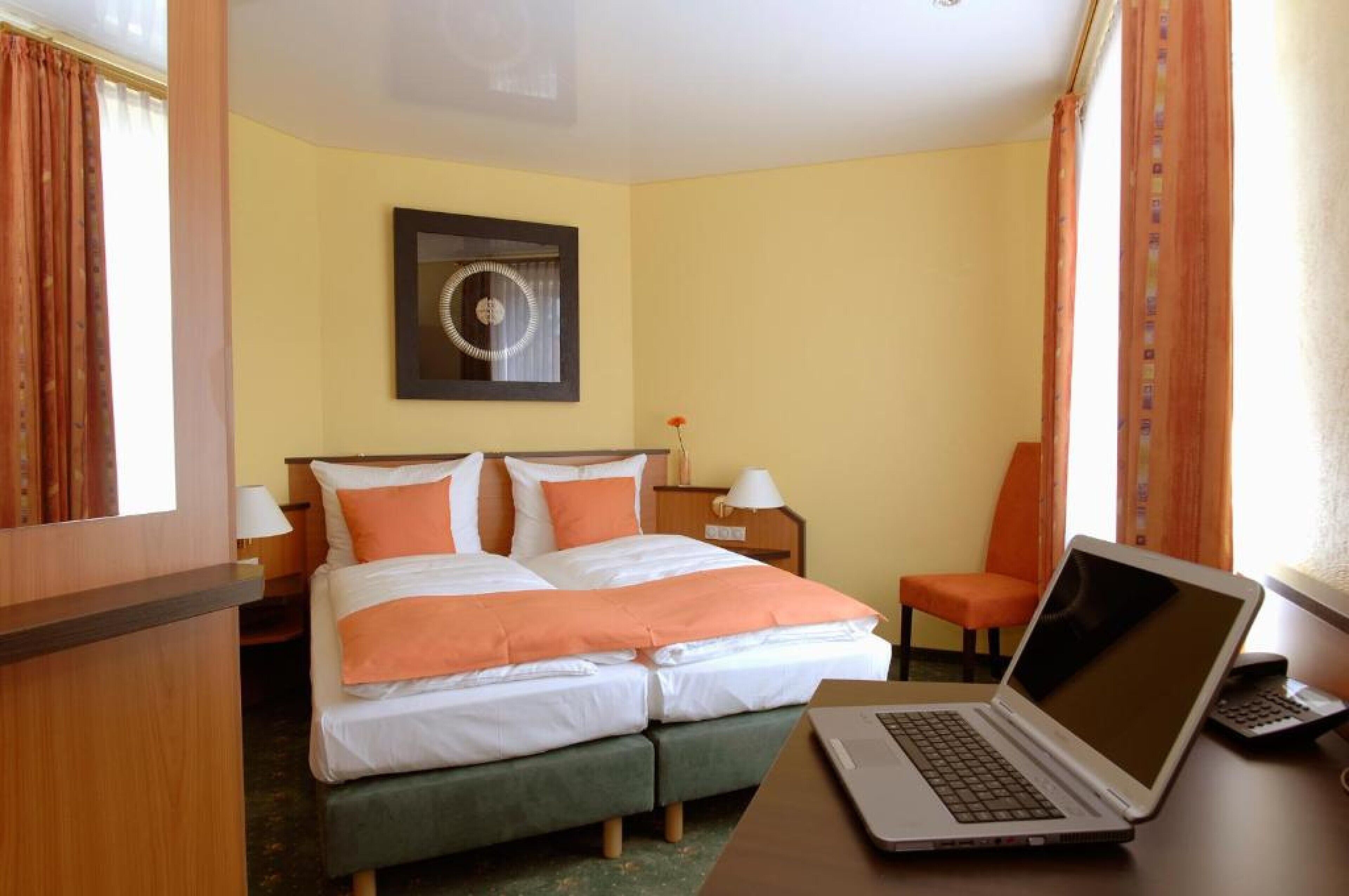 Ein Hotelzimmer mit Doppelbett, Schreibtisch mit Laptop, Stuhl, Nachttisch und einem an der Wand hängenden Bild.