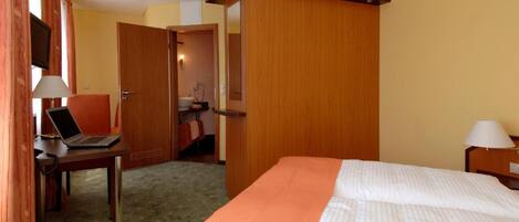 Una habitación de hotel con cama, un escritorio con una computadora portátil, un televisor y la puerta del baño.