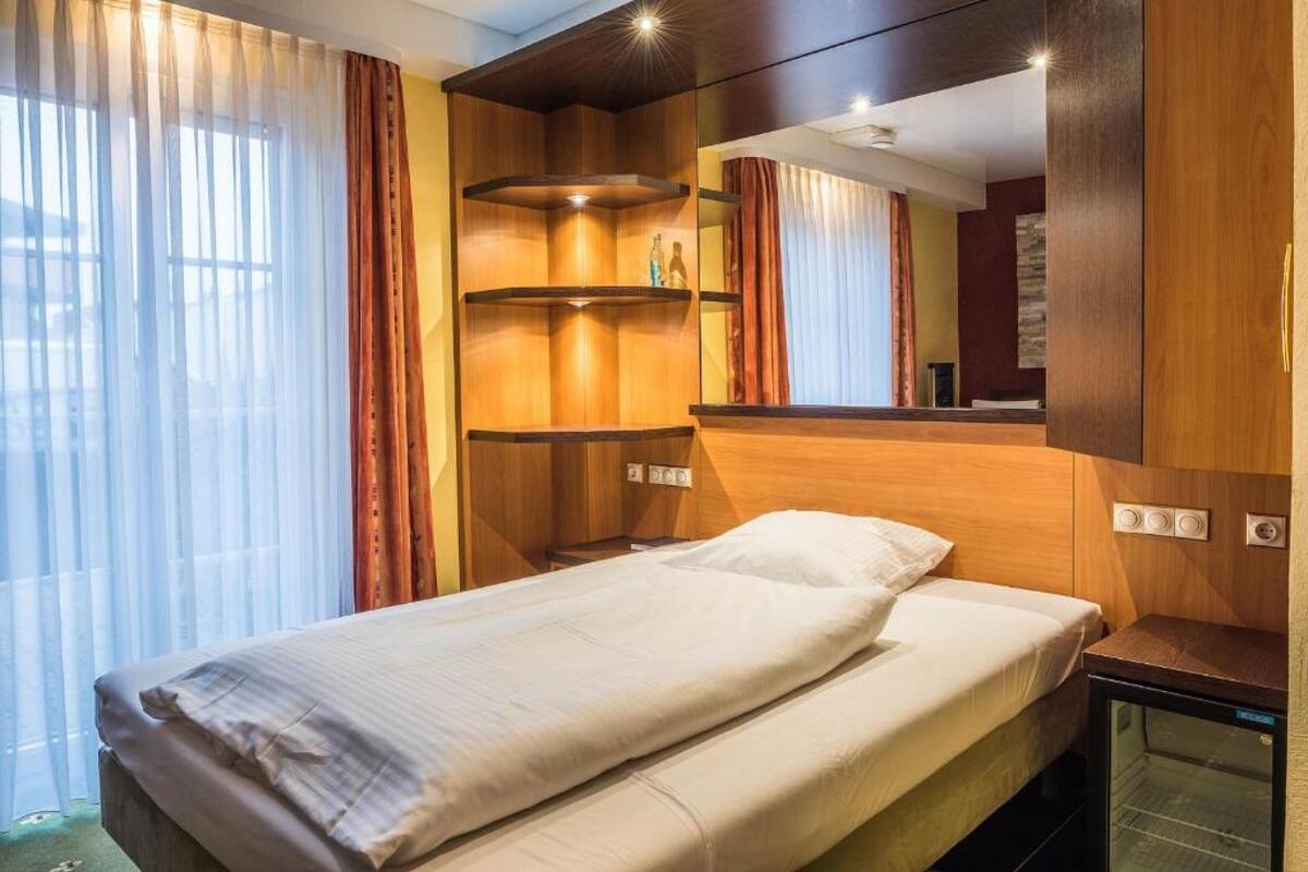 A hotel room with a bed, a mirror, a shelf with bottles, and a small table.