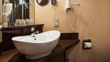 Un baño con lavamanos blanco, espejo, secador de pelo y dispensador de papel higiénico.