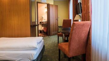 A hotel room with two beds, a desk with a chair, a television, and a bathroom visible through an open door.