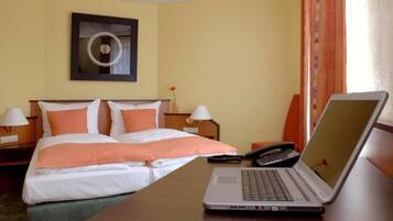 A hotel room with a bed, two bedside tables, a laptop, a phone, and a wall clock.