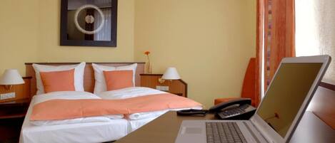 Habitación de hotel con una cama, dos mesitas de noche, una computadora portátil, un teléfono y un reloj de pared.
