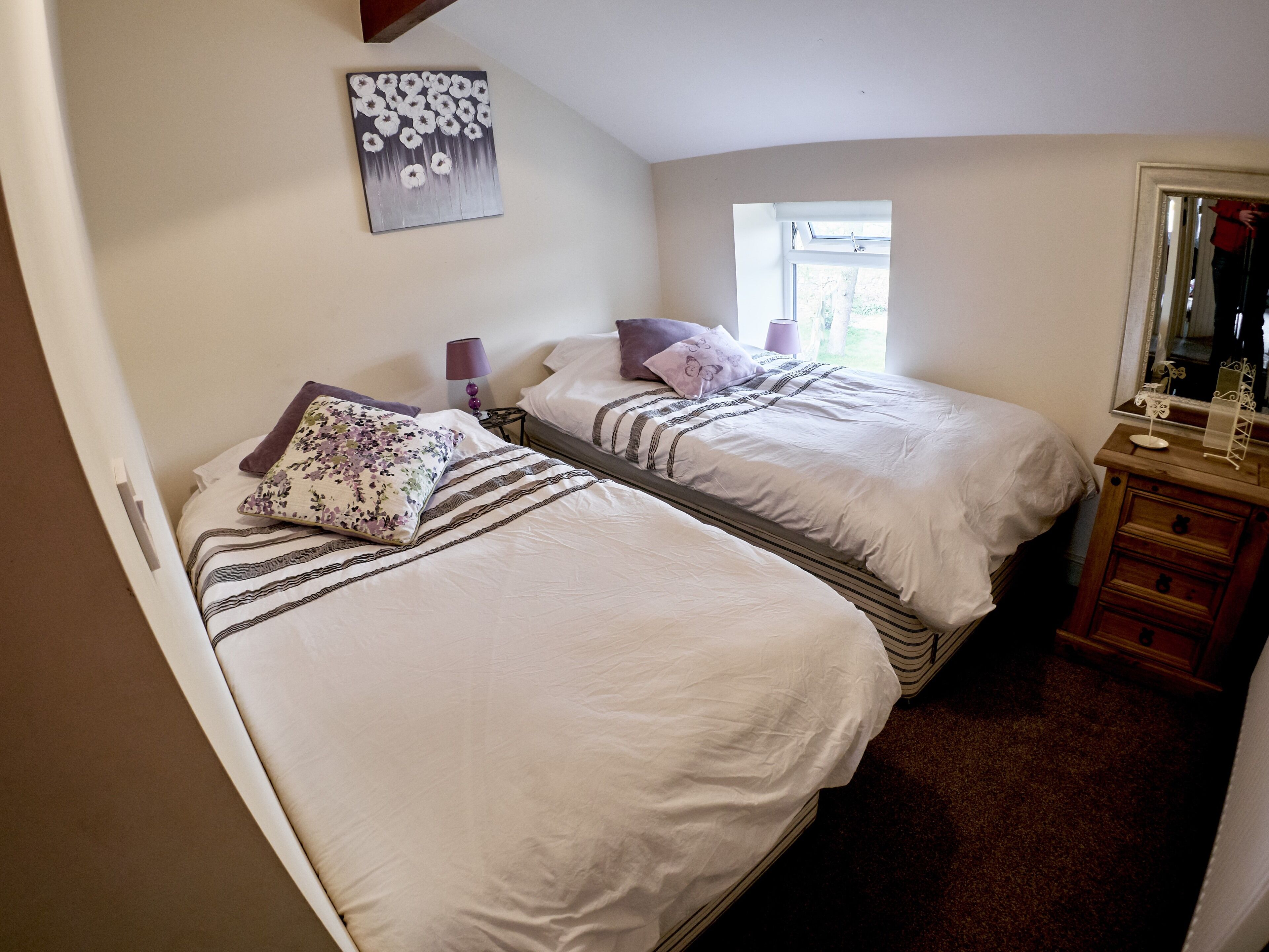A bedroom with two beds, a window, a dresser, and a painting on the wall.