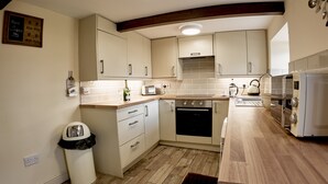 Une cuisine moderne avec un plancher en bois, des armoires blanches, un four encastré, un grille-pain et une machine à café.