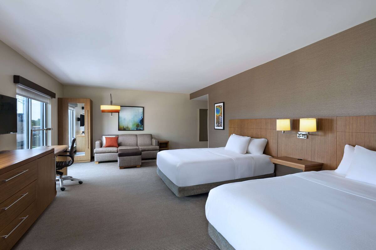 Ein Hotelzimmer mit zwei Betten, einem Schreibtisch, einem Sofa und einem Fernseher.