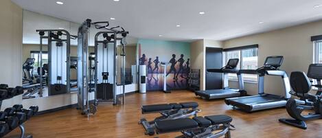 Un gimnasio con máquinas de cardio, bancos de pesas y un espejo grande.
