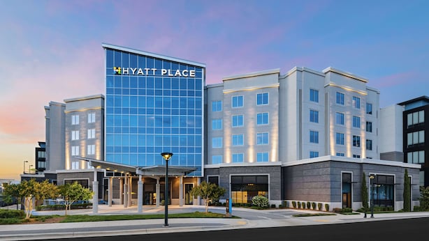 A modern hotel with a prominent glass facade, multiple entry points, and a landscaped entrance area.