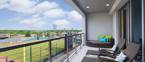 A balcony with wicker chairs and a sofa, overlooking a baseball field.
