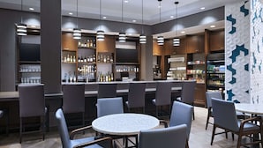 A modern bar area with round tables and bar stools, shelves with bottles, and a TV screen.