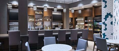 A modern bar area with round tables and bar stools, shelves with bottles, and a TV screen.