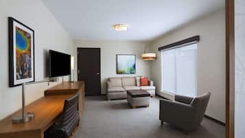 Habitación de hotel con escritorio, televisión de pantalla plana, sofá, sillón y ventana grande.