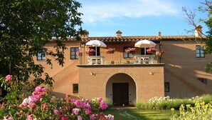 Un edificio de ladrillo de dos pisos con un balcón, un porche cubierto y un jardín con flores rosas y blancas.