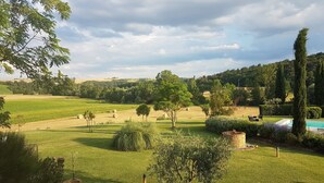 Un paisaje verde exuberante con colinas onduladas, cielo despejado y una zona de piscina con sillones de descanso.