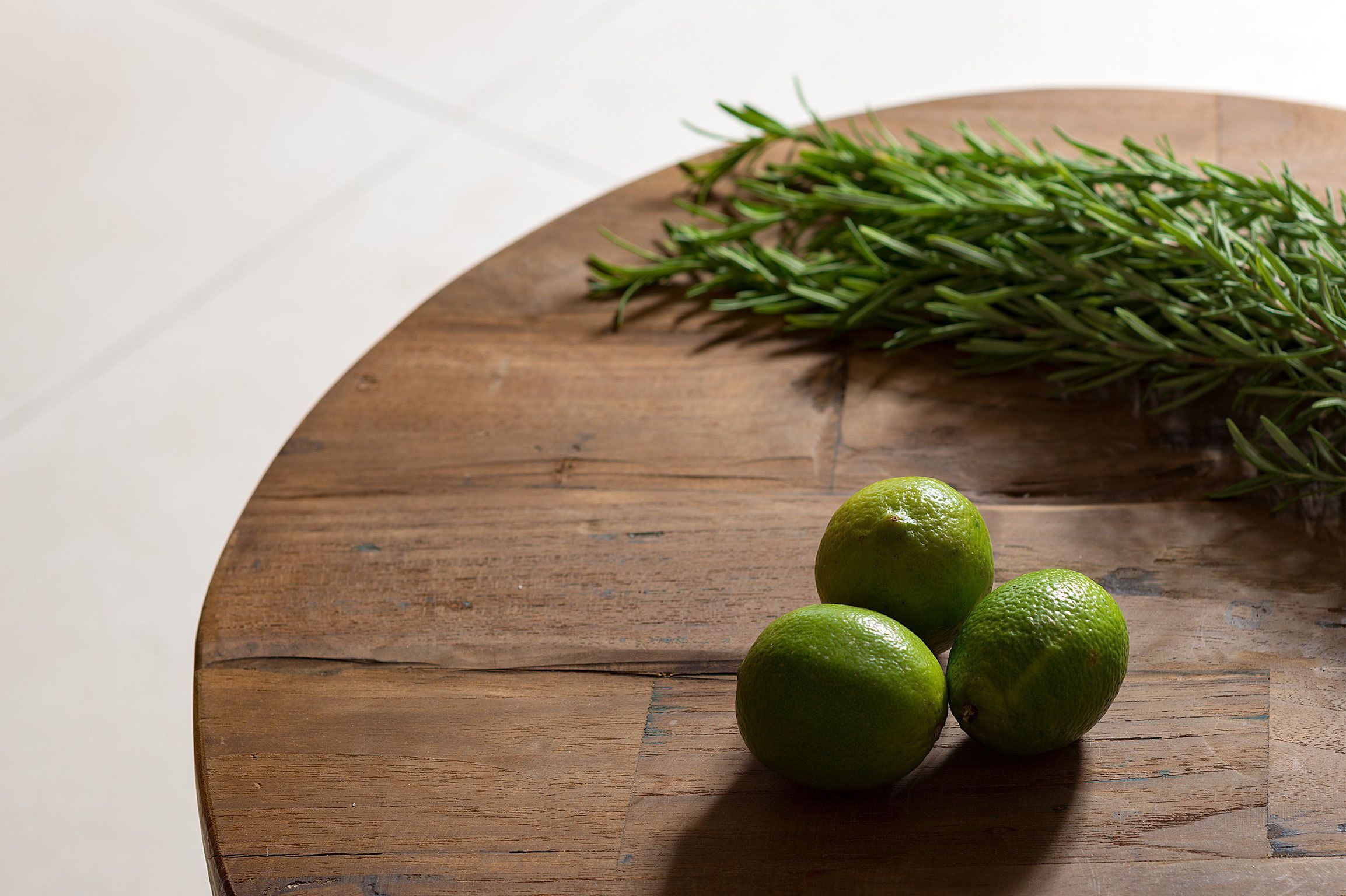 Una mesa de madera con tres limones verdes y una ramita de romero.