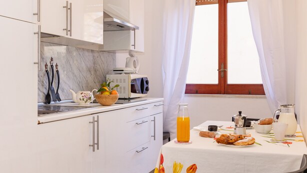 A modern kitchen with white cabinets, a marble countertop, and a breakfast table set with orange juice, pastries, and a teapot. - Residence Sorrento (Sorrento)