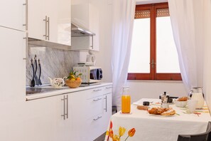 A modern kitchen with white cabinets, a marble countertop, and a breakfast table set with orange juice, pastries, and a teapot. - Residence Sorrento (Sorrento)