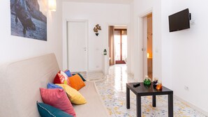 A living room with a sofa, colorful cushions, a small table, a flat-screen TV, and a wall-mounted lamp. - Residence Sorrento (Sorrento)