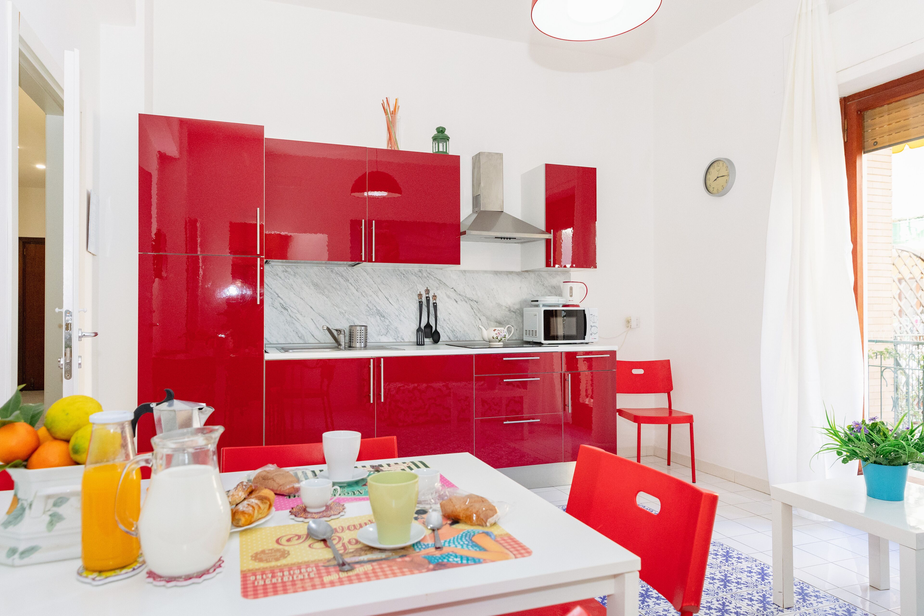 Una cocina moderna con armarios rojos, una encimera blanca y un comedor con una mesa dispuesta para el desayuno.
