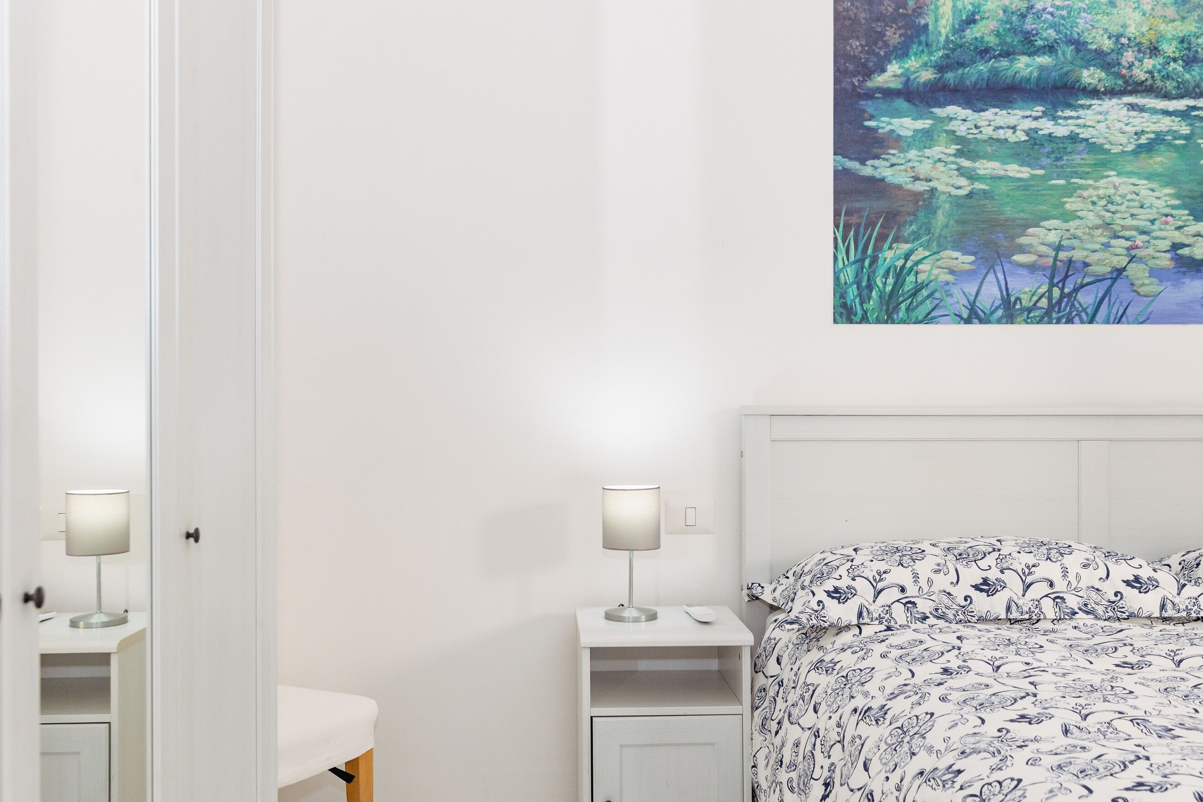 A bedroom with a bed, nightstands, a bedside table, and a wall-mounted painting of a pond.