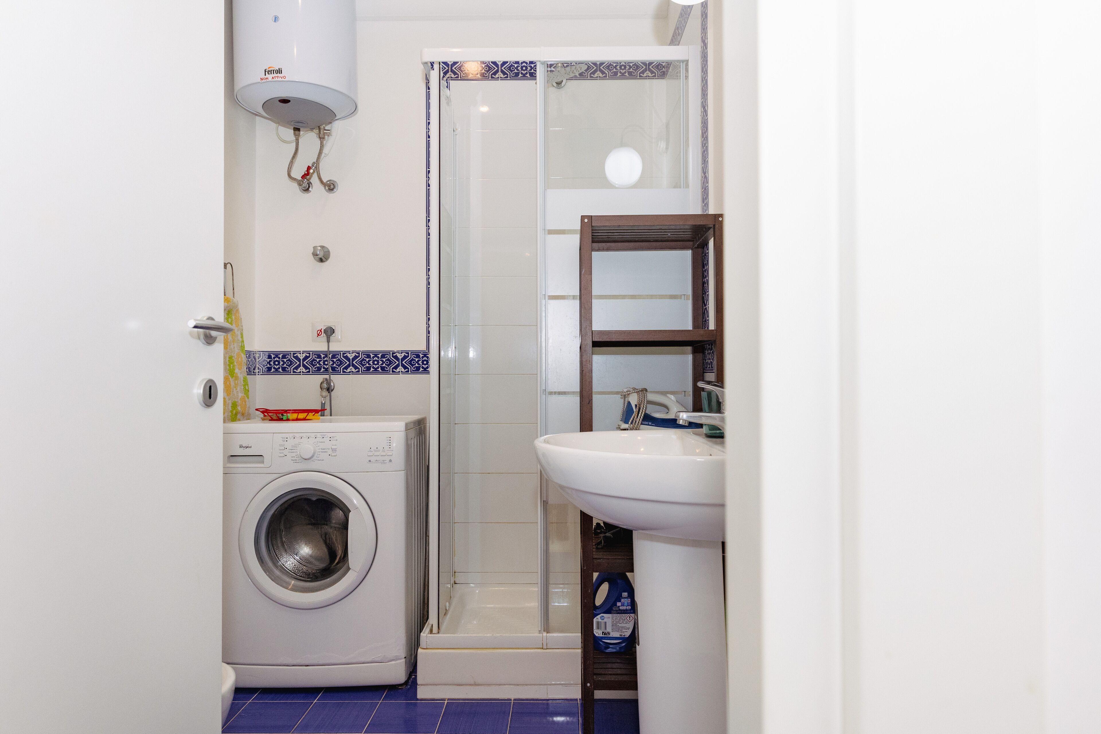 A compact bathroom with a washing machine, a glass-enclosed shower, and a sink.