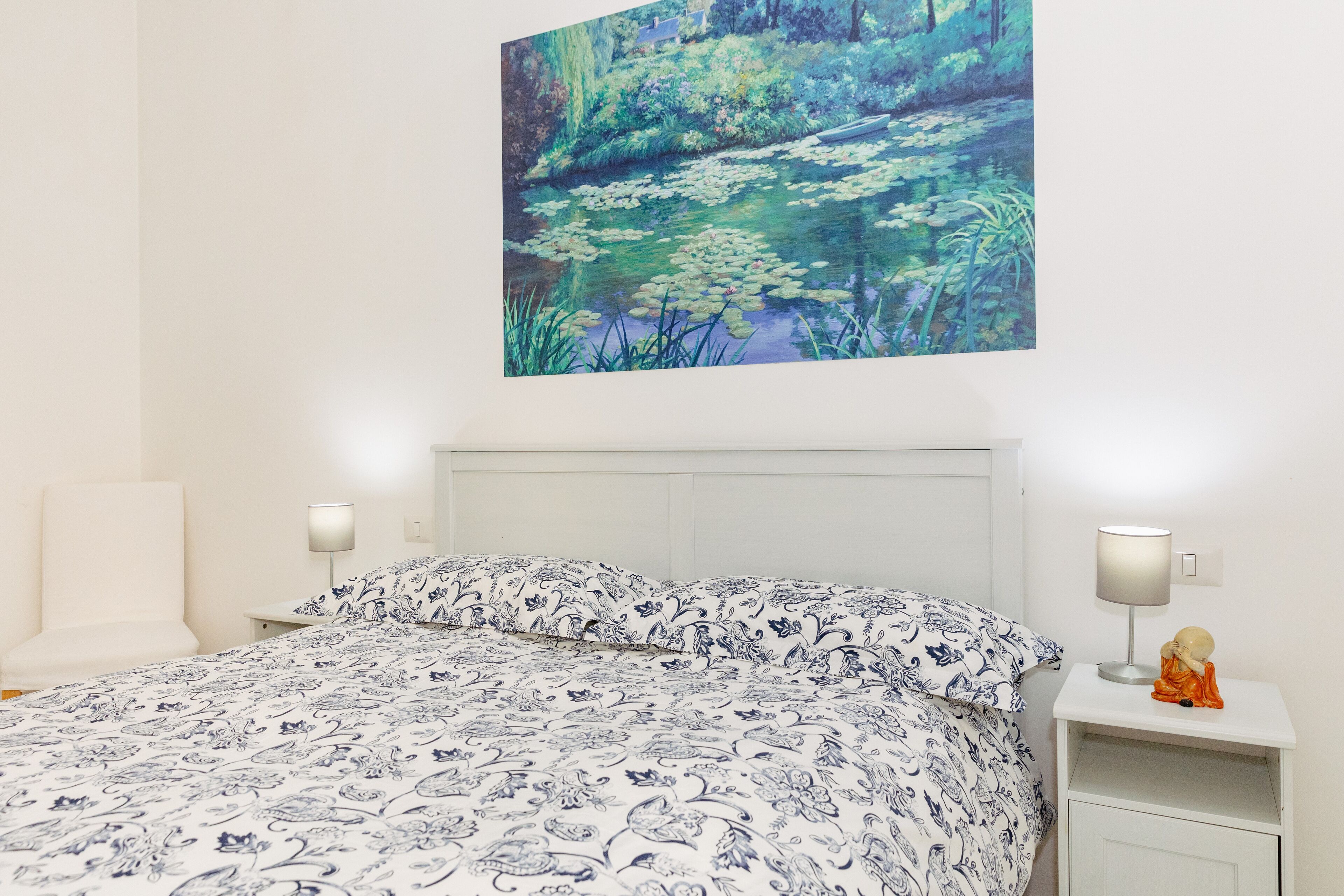 A bedroom with a bed, two bedside tables, and a wall-mounted painting of a pond.