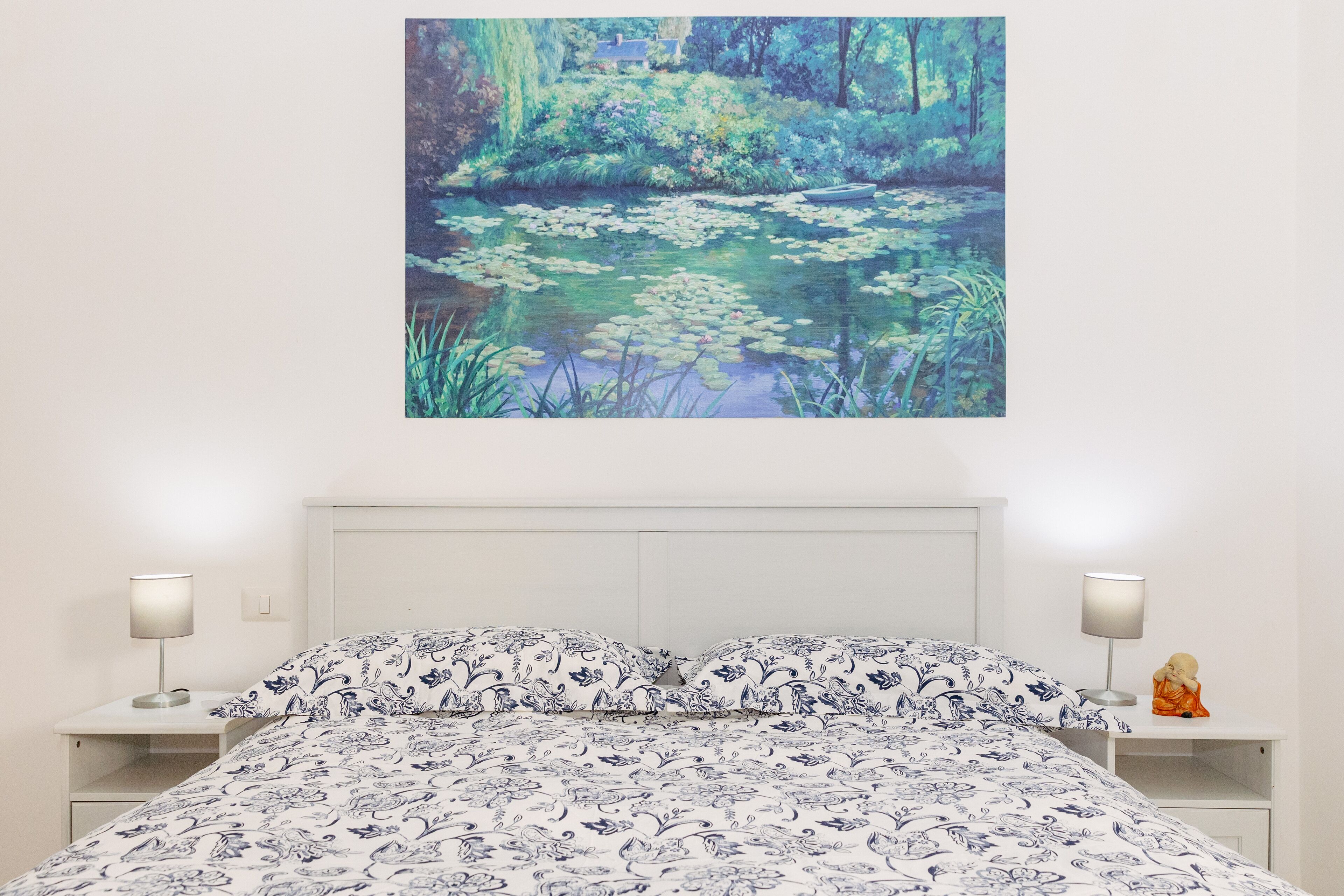 Une chambre à coucher avec un lit, deux tables de chevet et un tableau représentant un étang, accroché au mur.
