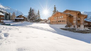 En snötäckt bergsby med hus byggda av trä, en klar himmel och en strålande sol.