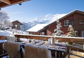 A wooden deck with a view of snow-covered mountains, a red building, and a wooden fence. - Chalet Sole - ski-in, ski-out (Wengen)