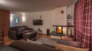 Ett modernt vardagsrum med en öppen spis, en soffgrupp, en tv och en mönstrad gardin.