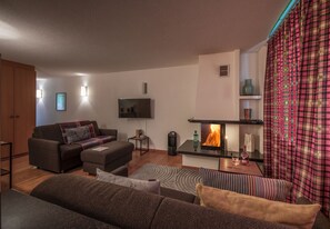 A modern living room with a fireplace, a sofa set, a television, and a patterned curtain. - Chalet Sole - ski-in, ski-out (Wengen)