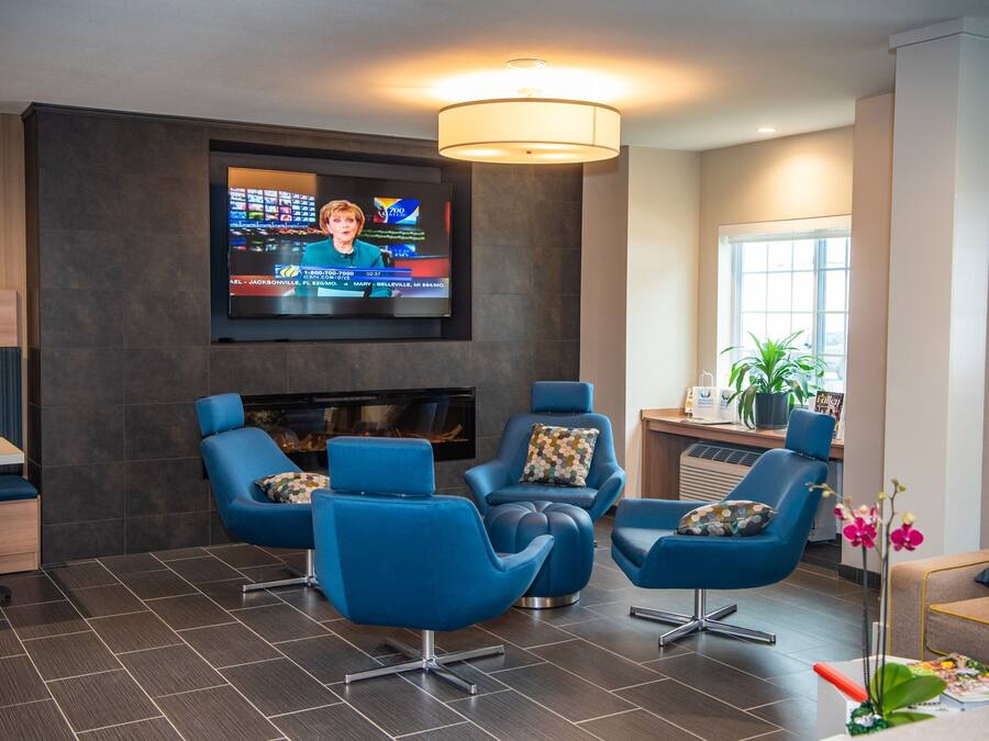 Ein moderner Lounge-Bereich mit einem Flachbildfernseher, blauen Sesseln, einem Kamin und einem großen Fenster.