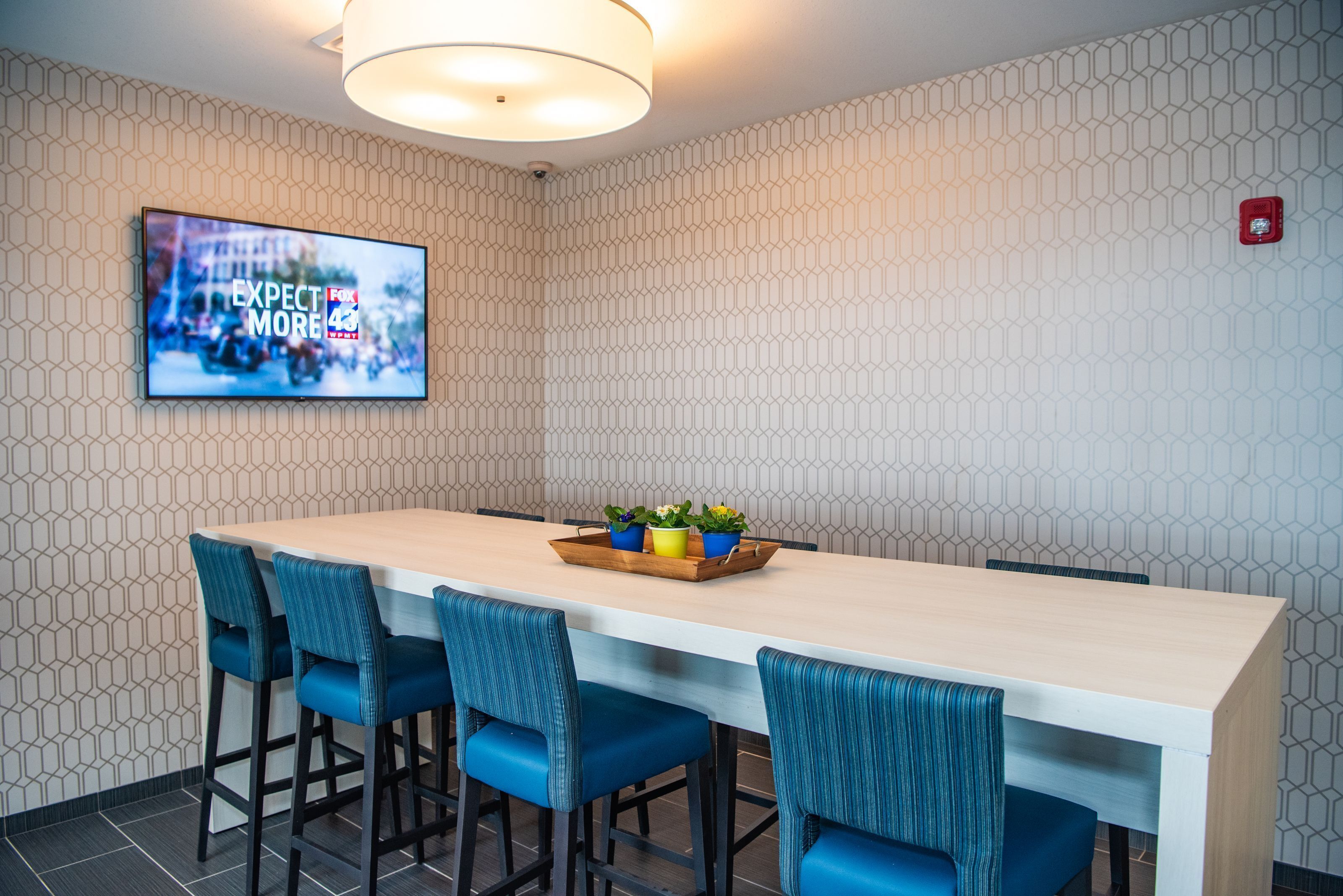A modern conference room with a long table, blue chairs, and a mounted TV displaying 'EXPECT MORE'.