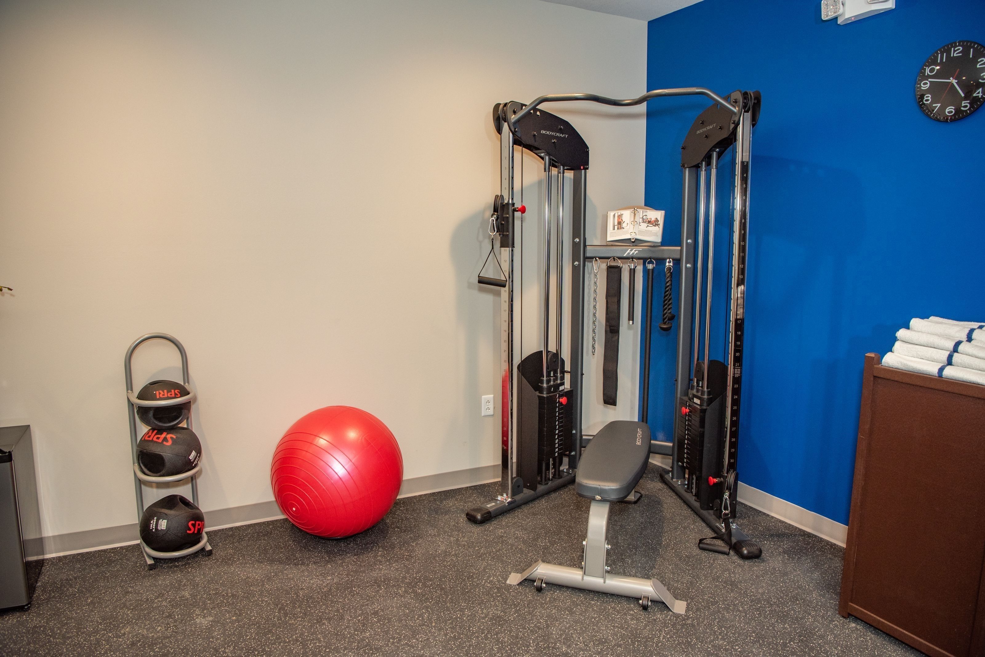 Une salle de sport équipée de matériel d’exercice, avec un ballon rouge et une horloge murale.