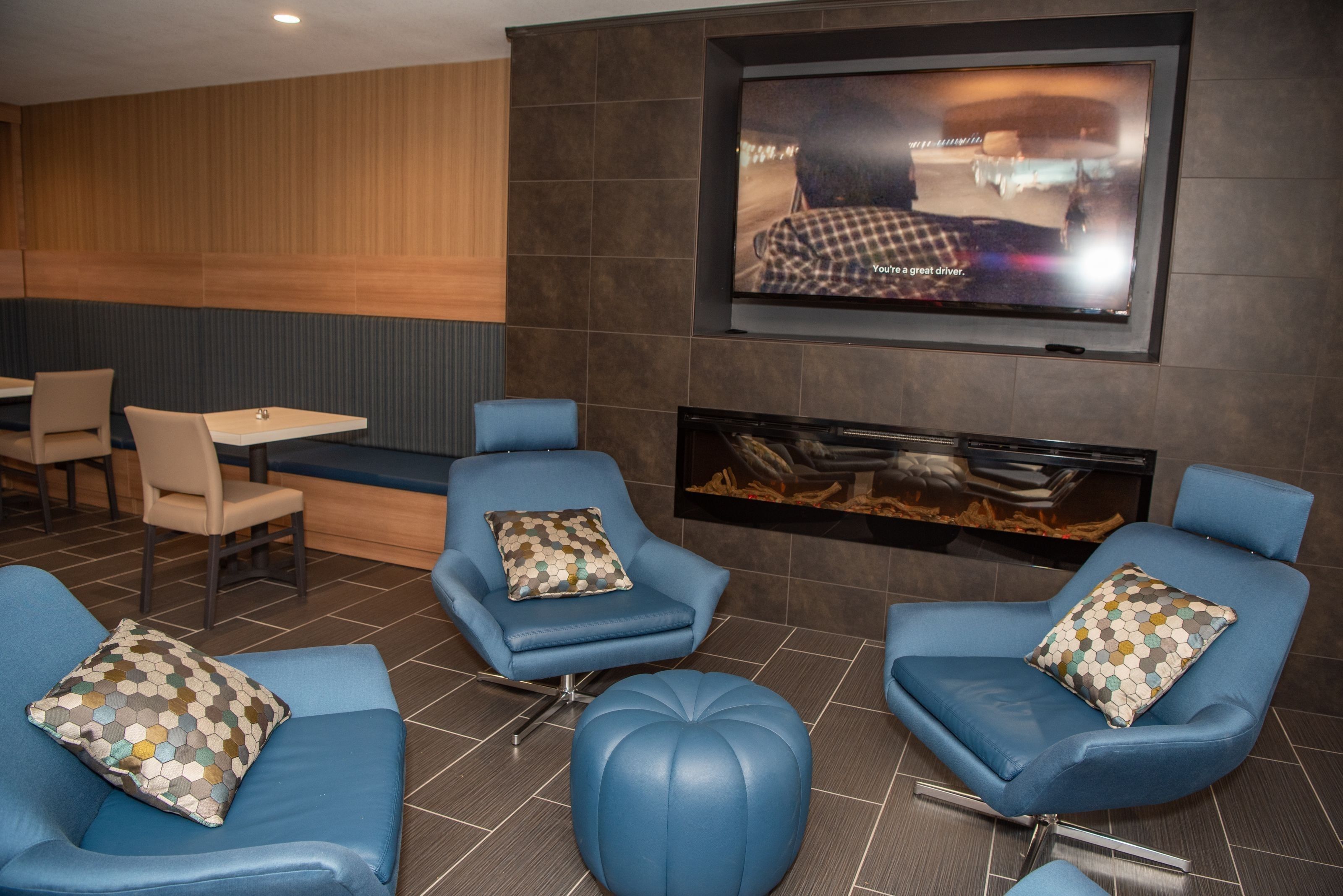 A modern lounge area with blue leather seating, a flat-screen TV mounted on the wall, and a fireplace.