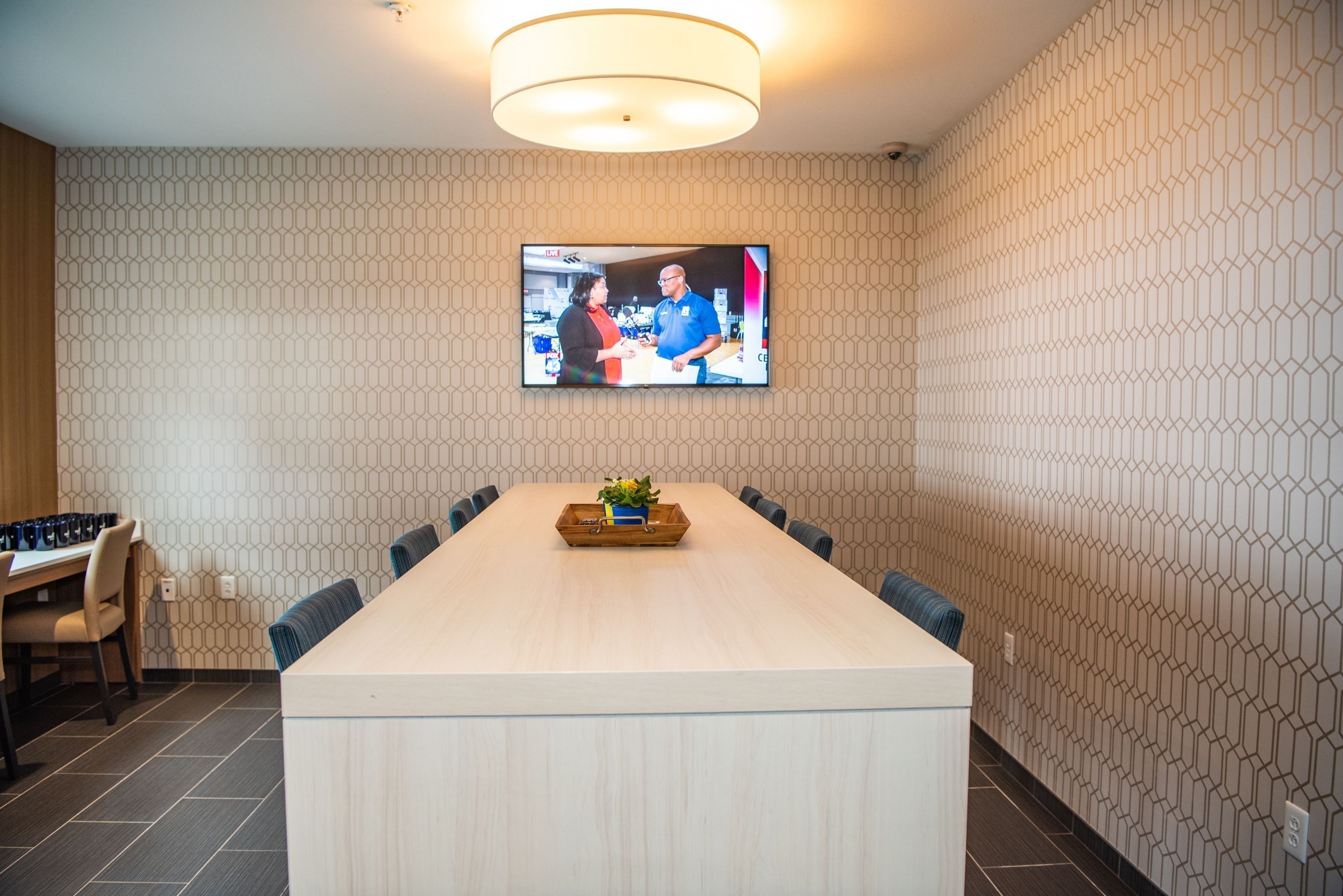 A conference room with a long table, chairs, a television mounted on the wall, and a patterned wall.