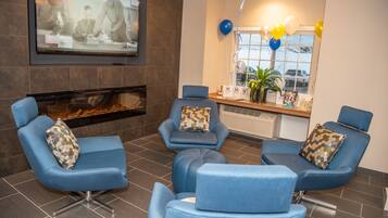 A modern waiting area with blue chairs, a fireplace, a television, and a window with balloons.