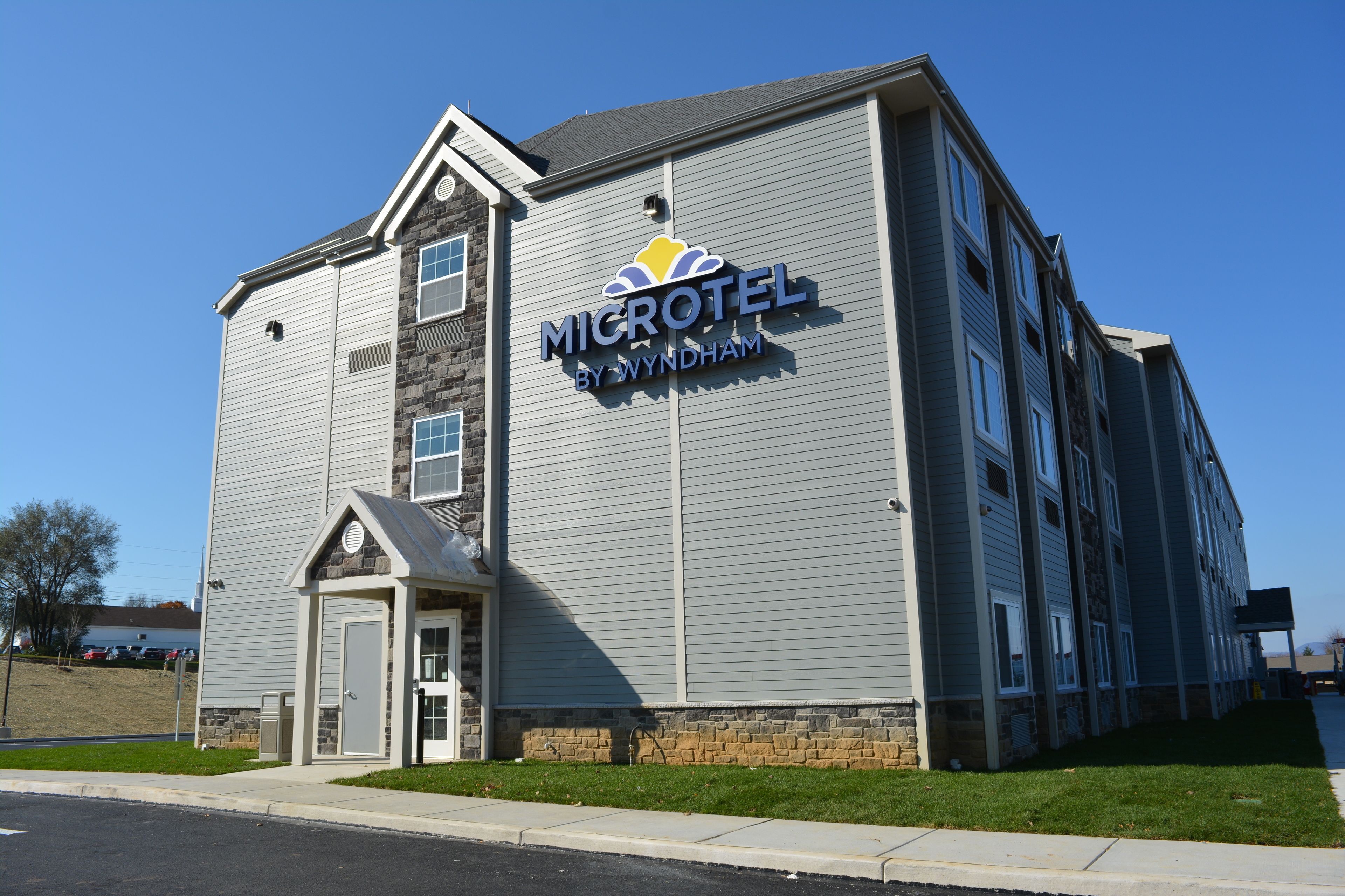 A two-story Microtel by Wyndham hotel with a stone facade, a small entrance, and a clear blue sky in the background.