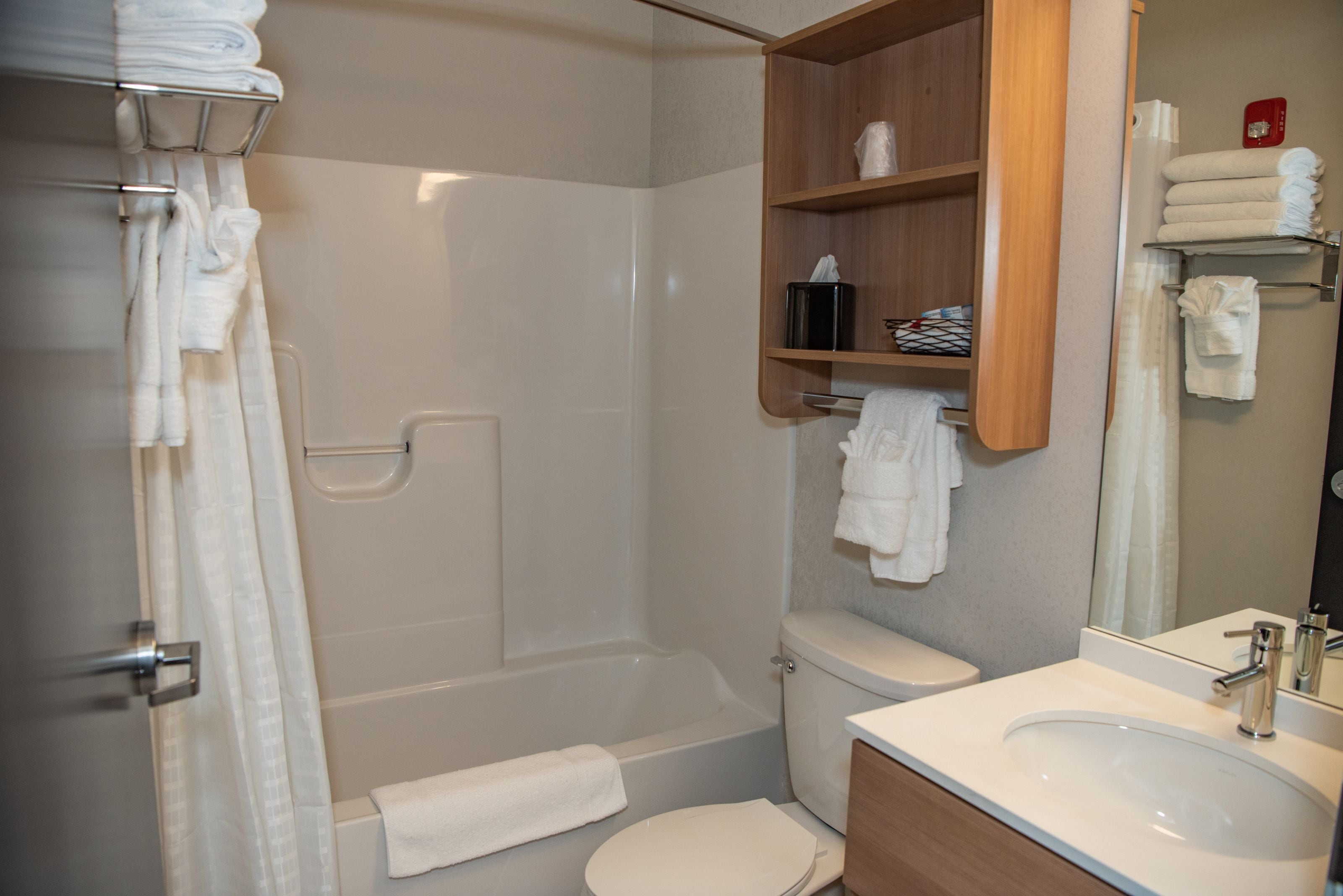 Un baño moderno con bañera, inodoro y lavamanos. Hay toallas y artículos de aseo en estantes.