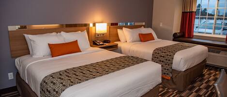 A hotel room with two beds, a nightstand with a lamp, a window with curtains, and a view of parked cars outside.