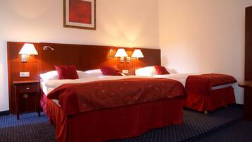 Habitación de hotel con dos camas, cada una con ropa de cama y cabeceros rojos. Hay dos lámparas de noche y un cuadro en la pared.