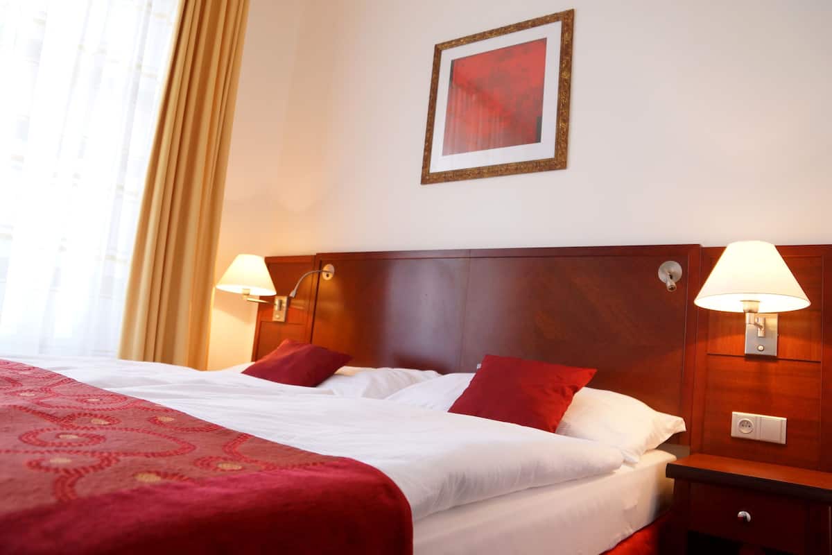 Una habitación de hotel con una cama grande, dos lámparas de noche, un cuadro en la pared y una ventana con cortinas.
