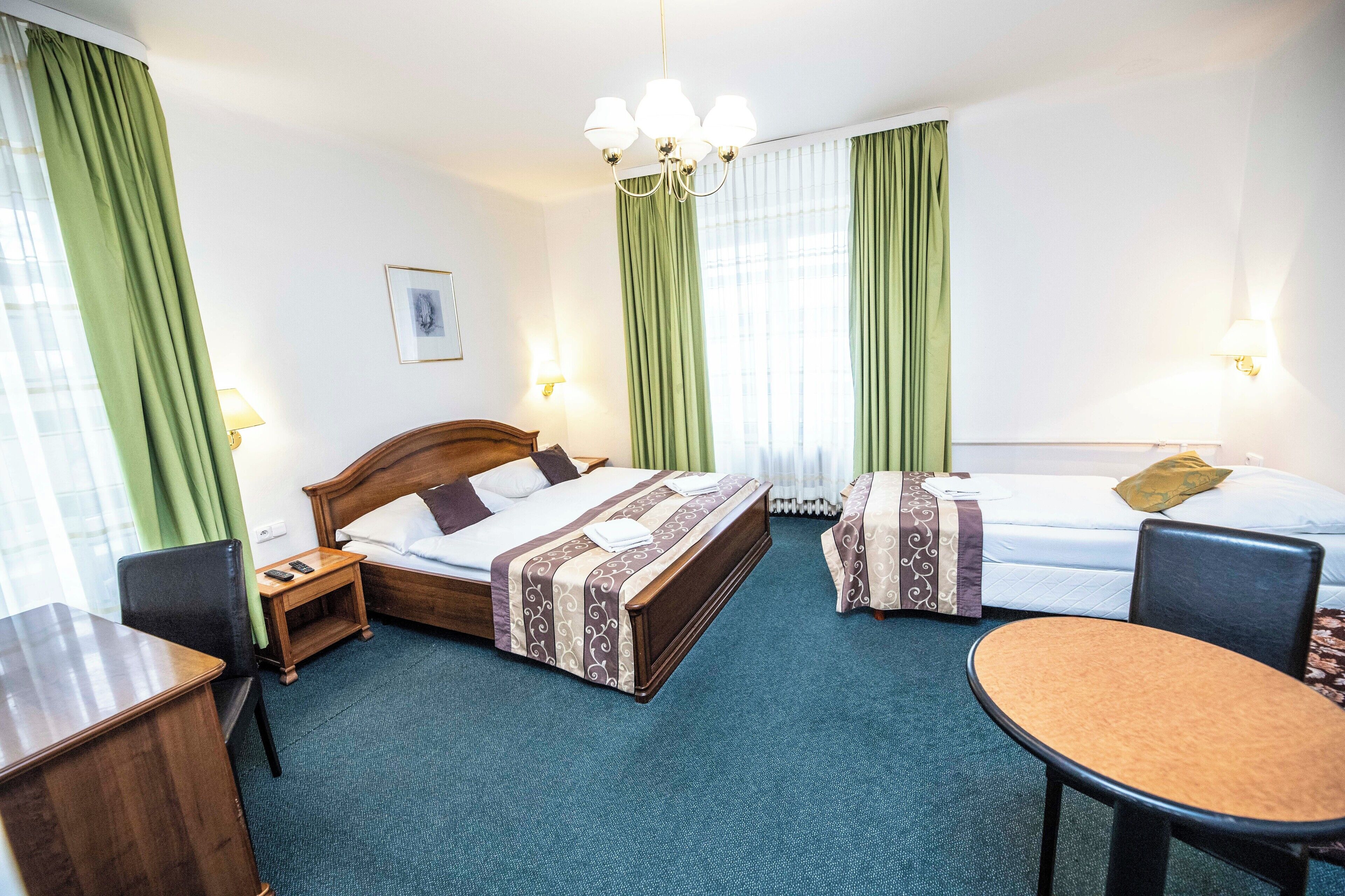 A hotel room with a bed, a desk, a chair, and a small table.
