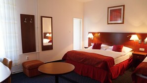 A hotel room with a bed, bedside tables, a round table, a mirror, and a wall-mounted picture.