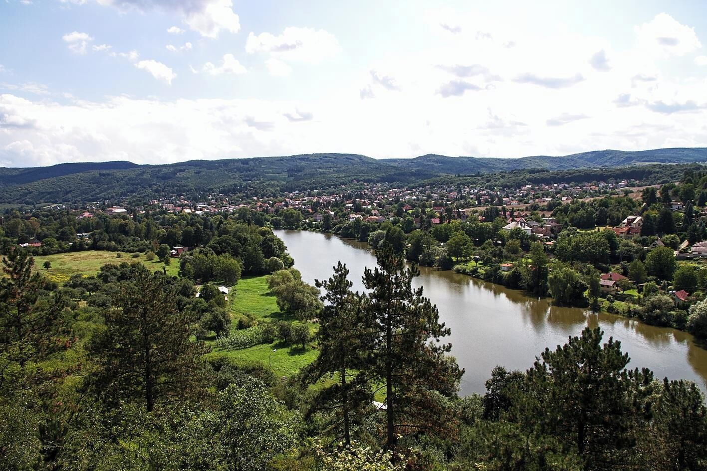 A river flowing through a town with surrounding greenery and hills in the background.