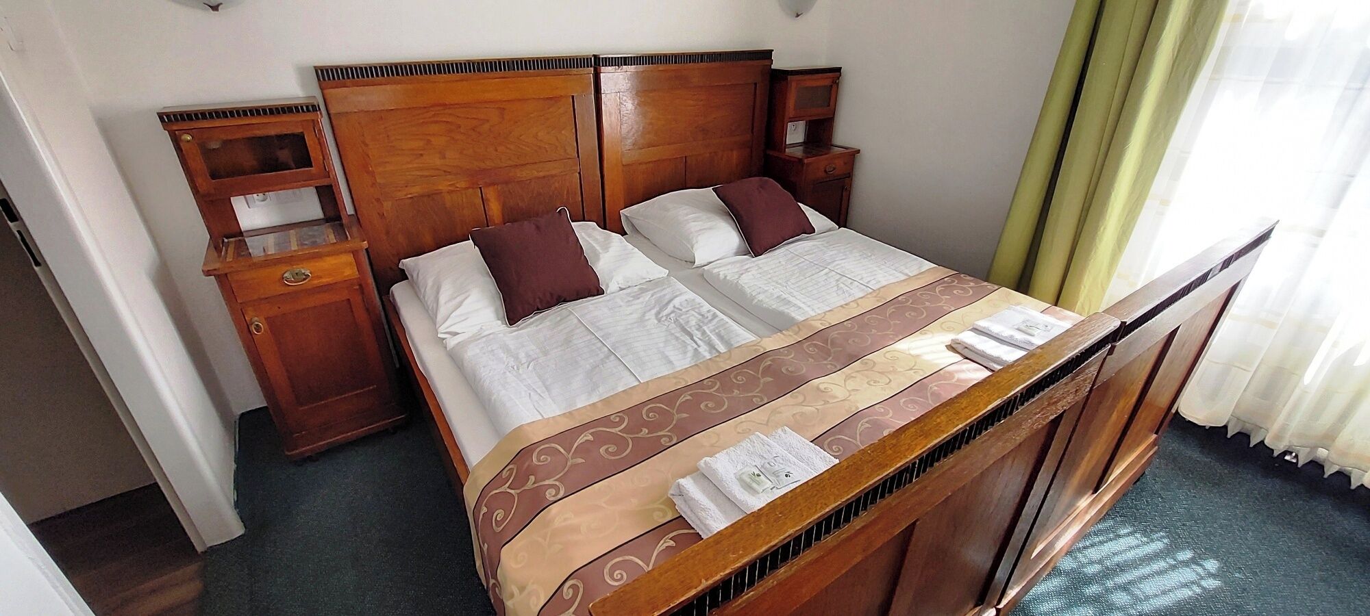 A hotel room with a wooden bed, two bedside tables, and a window with curtains.